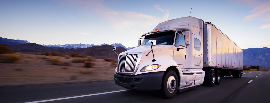 A white truck driving down the road near some mountains.